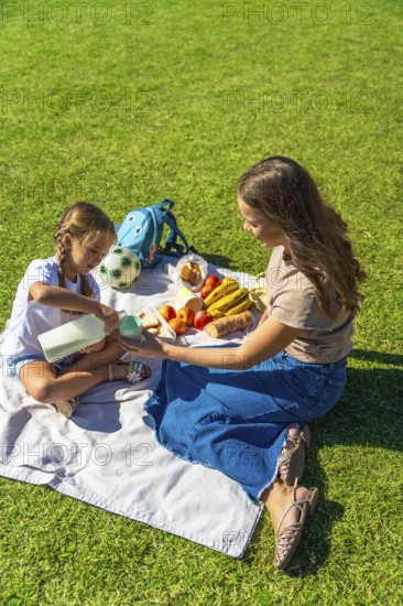 Mother and daughter enjoying a summer picnic in a lush green park, sharing healthy food, fruit, and milk in a natural environment, fostering family connection and wellness