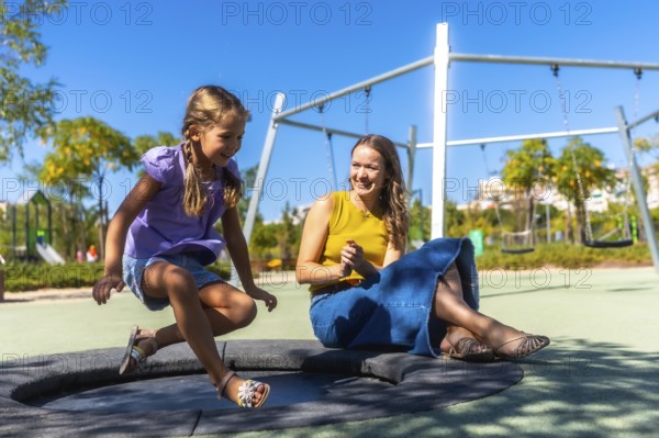 Mother and daughter enjoying time together, bonding and laughing while playing on an outdoor trampoline in a sunny park playground during summer vacation