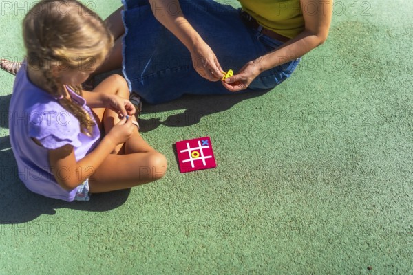 Mother and daughter bonding over a game of tic tac toe on a sunny day, enjoying quality family time and childhood leisure activities in a park setting