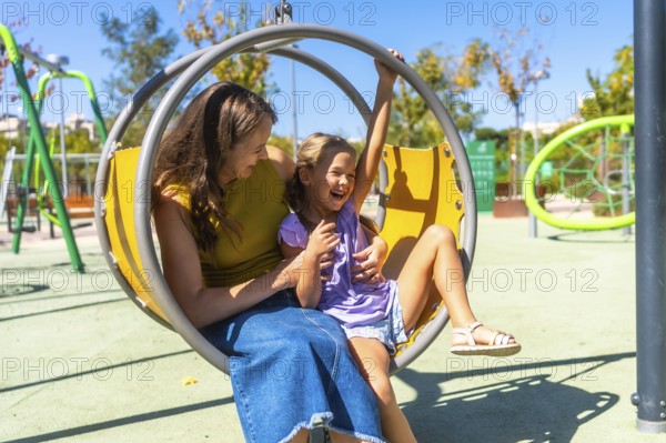Mother and daughter enjoying time together on a colorful playground swing, laughing and sharing a happy moment filled with joy and childhood memories on a sunny day