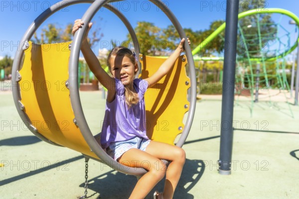 Young girl smiling on a modern oversized swing at a sunny outdoor playground, enjoying carefree summer playtime, energy and joy in a bright, happy park setting