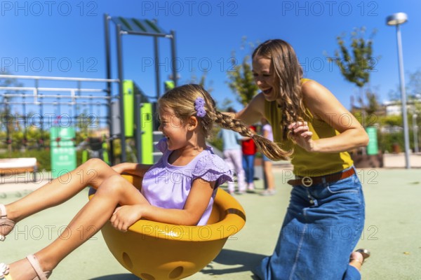 Mother and daughter laughing on a sunny playground spinner, sharing carefree bonding and joyful playtime outdoors, summer family moment of love and laughter