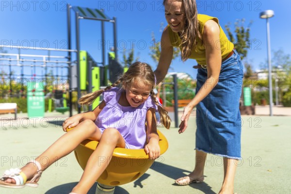 Mother and daughter laughing on a colorful spring rider at a sunny outdoor playground, sharing a joyful summer moment of bonding, play and carefree childhood happiness