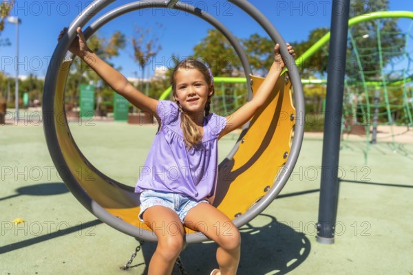 Happy child swinging on a round playground swing, enjoying outdoor activity on a sunny day, experiencing joy and carefree childhood moments at the park