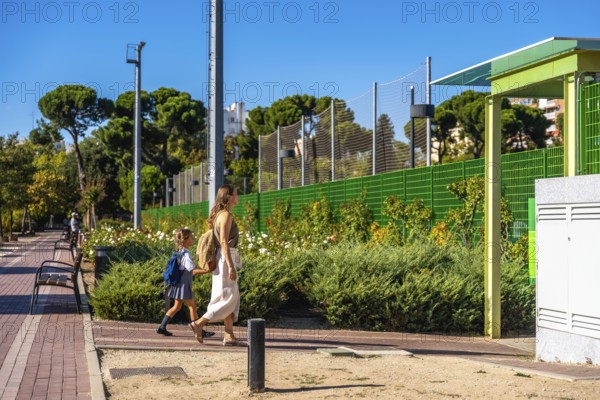 Mother and daughter walking together on a sunny day, the young student wearing a backpack and uniform, heading towards school, symbolizing education, family support, and a new school year