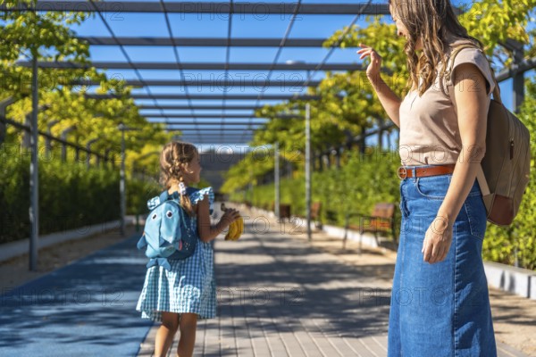 Woman and young girl walking along a path surrounded by lush green foliage and a modern pergola, a mother saying goodbye to her daughter before school