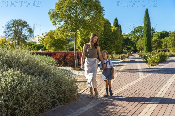 Mother and daughter walking along a path in a park, holding hands and going to school on a sunny day, representing family, education, and early childhood