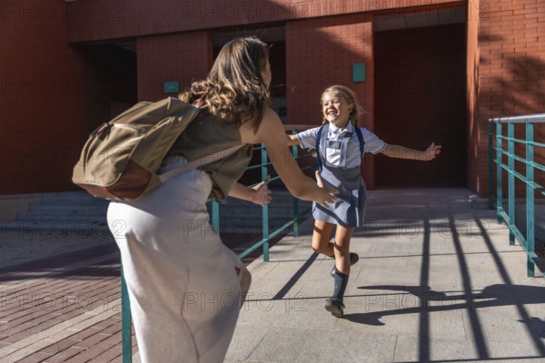 Mother and daughter joyfully reuniting for a hug outside the school building, the happy schoolgirl running towards her parent after finishing the day, symbolizing family love and education