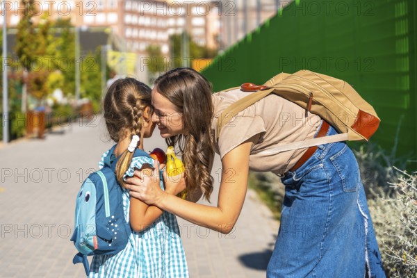 Loving mother bending down to embrace her small daughter with a backpack on the first day of school, showing care and emotional connection as the child prepares for new learning