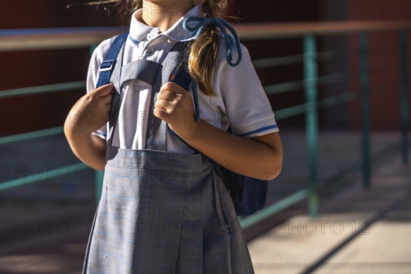 Young student in school uniform stands outdoors on a sunny day holding a backpack, ready and prepared for the first day of classes and a new academic year
