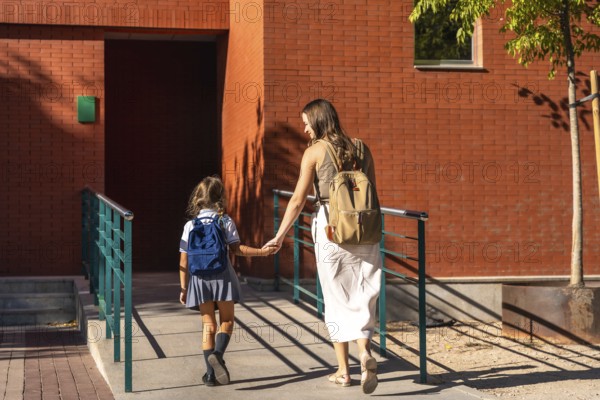 Mother and daughter walk uphill hand in hand with backpacks, returning to schoolbonding, support and preparation for a new school year on a sunny day