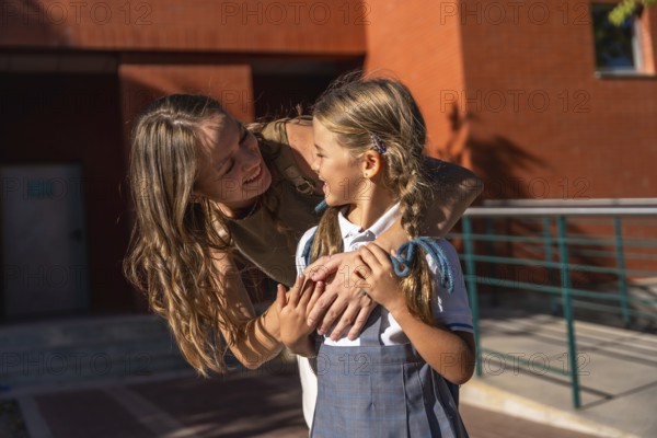 Woman tenderly hugging her daughter wearing a school uniform, sharing a loving moment outside the school building, symbolizing back to school and family support