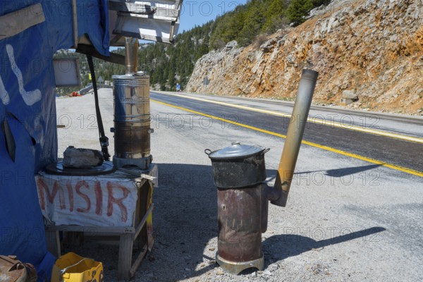 Temporary stand with ovens on the side of the road in mountainous surroundings, on the left traditional samovar, kettle for making tea, powered by wood, on the right portable oven with cooking pot, powered by wood, selling cooked corn on the side of the road on the D695 near Akseki, Antalya province, Turkey