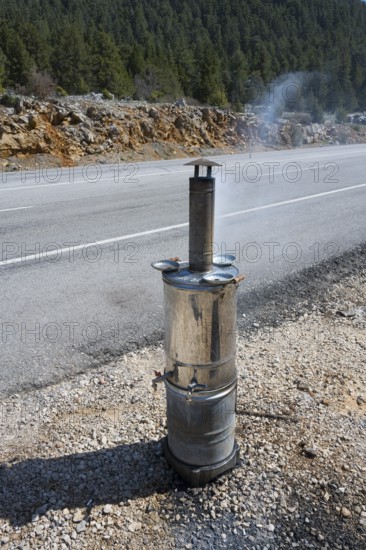 Smoking metal stove with roadside chimney against wooded backdrop, traditional samovar, kettle for making tea, powered by wood, on the side of the road on the D695 near Akseki, Antalya province, Turkey