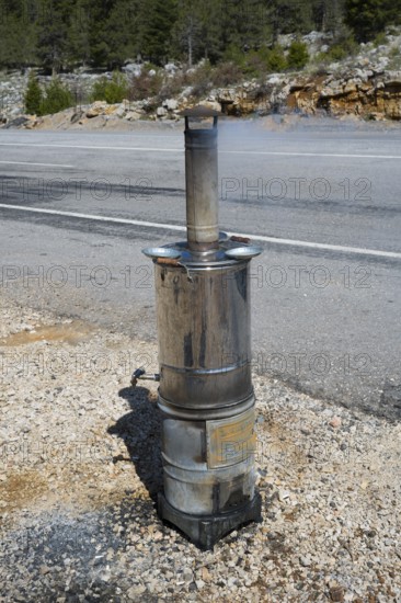 Metal stove with chimney stands on the side of the road against a wooded backdrop, traditional samovar, kettle for making tea, powered by wood, on the side of the road on the D695 near Akseki, Antalya province, Turkey