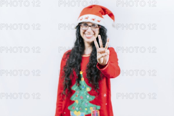 Happy girl in Christmas hat counting number THREE, isolated. Smiling girl in Christmas sweater counting number 3