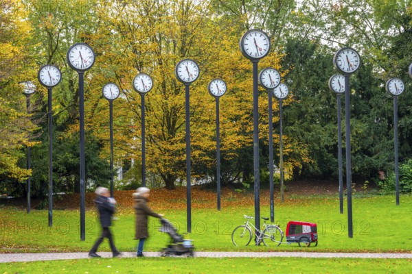 The art installation Zeitfeld in Volksgarten Park in Düsseldorf-Oberbilk, a total of 24 station clocks, on 6 meter high steel columns, have been running synchronously since 1987, walkers in the municipal park, artwork by Düsseldorf artist Klaus Rinke, symbol of time, time change, North Rhine-Westphalia, Germany