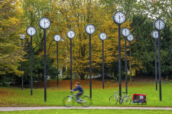 The art installation Zeitfeld in Volksgarten Park in Düsseldorf-Oberbilk, a total of 24 station clocks, on 6 meter high steel columns, have been running synchronously since 1987, cyclists in the municipal park, artwork by Düsseldorf artist Klaus Rinke, symbol of time, time change, North Rhine-Westphalia, Germany