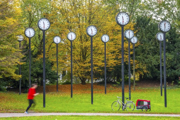 The art installation Zeitfeld in Volksgarten Park in Düsseldorf-Oberbilk, a total of 24 station clocks, on 6 meter high steel columns, have been running synchronously since 1987, jogger in the municipal park, artwork by Düsseldorf artist Klaus Rinke, symbol of time, time change, North Rhine-Westphalia, Germany