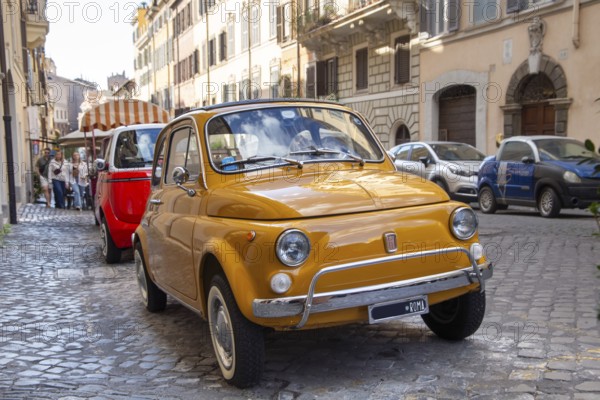 A yellow Fiat 500 is parked in an alley in central Rome