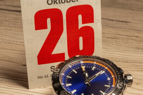 Wintertime 2025 time change: Close-up of a wristwatch and a sheet of a tear-off calendar showing the date October 26