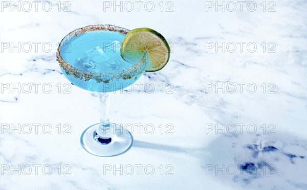 Bright blue cocktail with a slice of lime on a marble surface