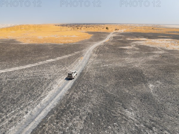 Aerial view of off-road car driving on a salt pan, arid landscape, Botswana