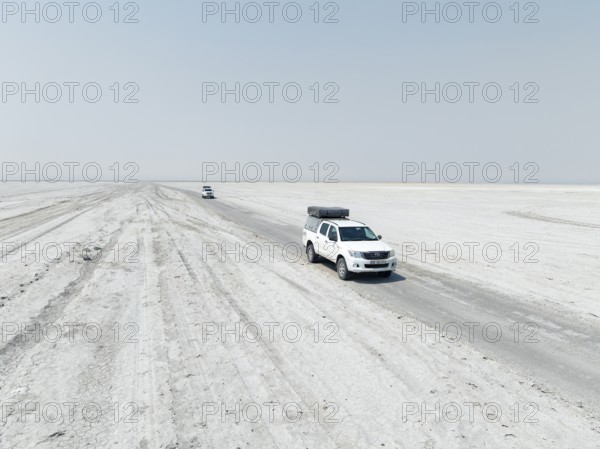 Aerial view, two off-road cars driving on a salt pan, arid landscape, Botswana