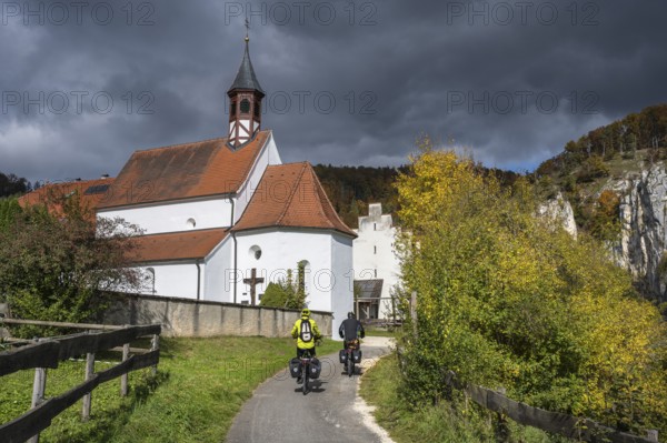 Cyclists on the Danube Valley Cycle Path in front of St. George's Basilica at Käppeler Manor near Thiergarten in the Upper Danube Valley, surrounded by autumn vegetation, Sigmaringen district, Baden-Württemberg, Germany
