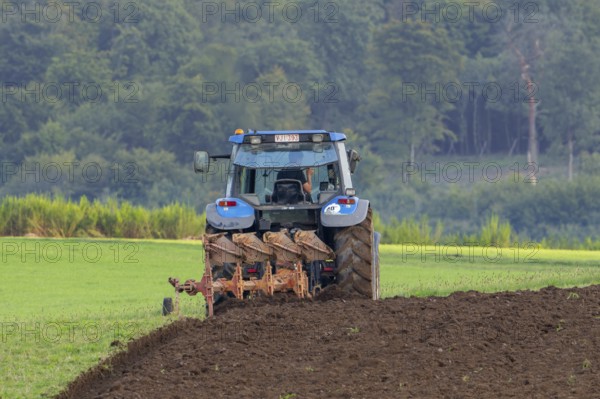 Tractor with plough, agricultural ploughing machine working on a field in autumn, fall in the Belgian Ardennes, Luxembourg, Wallonia, Belgium