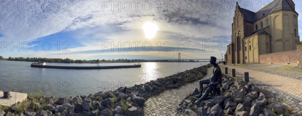 Photo with melancholy mood of bronze sculpture Poortekerl looking at Rhine waiting for ship to unload, Rhine navigation inland navigation, reminiscence of old times, bronze statue by artist Heide Friede-Kinalzik, rebuilt church of St. Martini destroyed in the Second World War, Emmerich, Lower Rhine, North Rhine-Westphalia, Germany