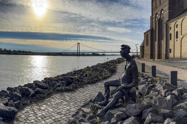 Photo with melancholy mood of bronze sculpture Poortekerl looking at Rhine waiting for ship to unload, Rhine navigation inland shipping, reminiscence of old times, bronze statue by artist Heide Friede-Kinalzik, Emmerich, Lower Rhine, North Rhine-Westphalia, Germany