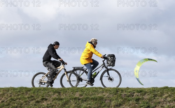 Cyclists ride across a dike and look at the sails of kite surfers, Fehmarn, 16.10.2025, Fehmarn, Schleswig-Holstein, Germany