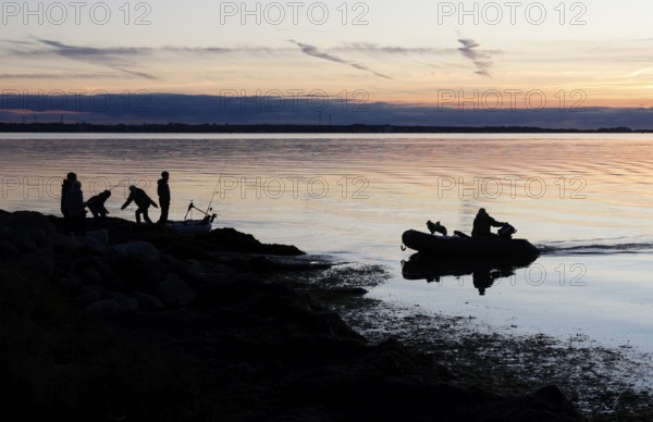 Angler on the beach during sunset, an angler docks on the shore with his inflatable boat and dog, Fehmarn island, 18.10.2025, Fehmarn, Schleswig-Holstein, Germany