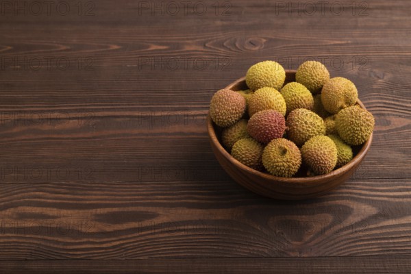 Ripe Lychee on clay bowl on brown wooden background, side view, copy space, minimalism