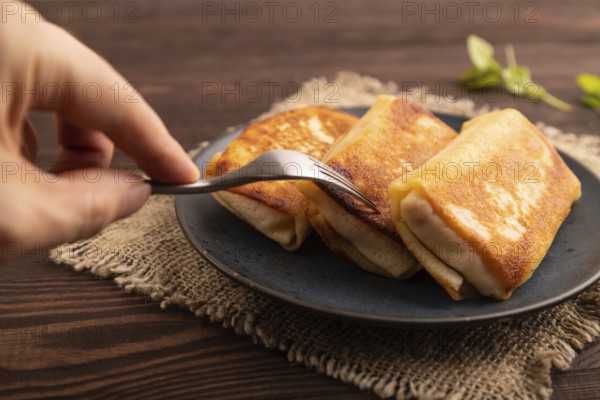 Fried crispy pancakes with meat and cheese with hand on brown wooden background and linen textile. side view, close up, selective focus