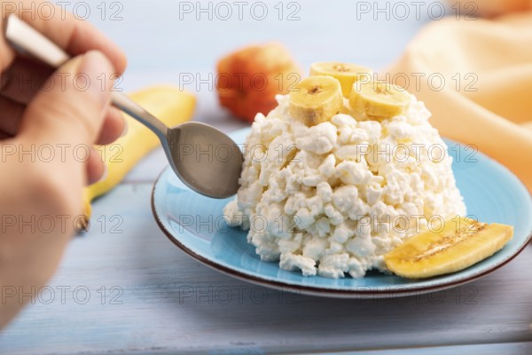 White ?ottage cheese, Curd, with Banana with hand on blue wooden background and orange textile, side view, close up, selective focus