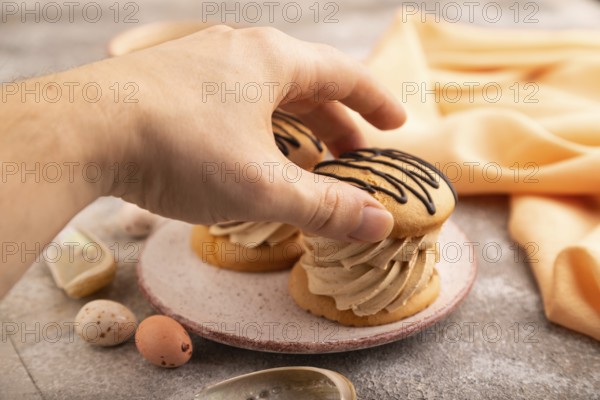 Caramel Cream Cakes with hand on brown concrete background, cup of coffee, side view, close up, selective focus