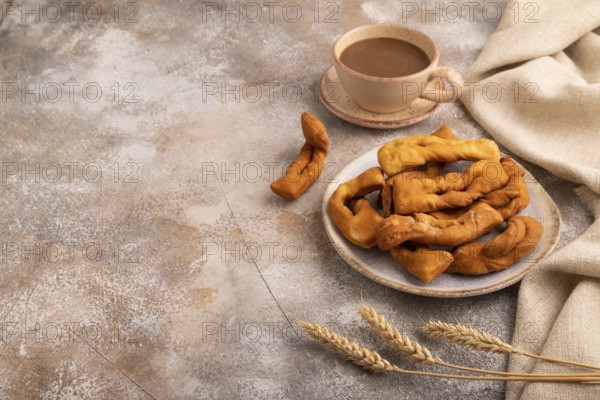 Crunchy biscuit Brushwood cookies sprinkled with powdered sugar on brown concrete background and linen textile, cup of coffee, side view, copy space