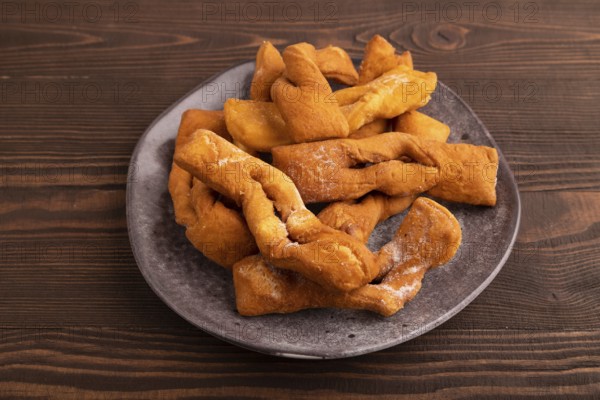 Crunchy biscuit Brushwood cookies sprinkled with powdered sugar on brown wooden background, side view, close up