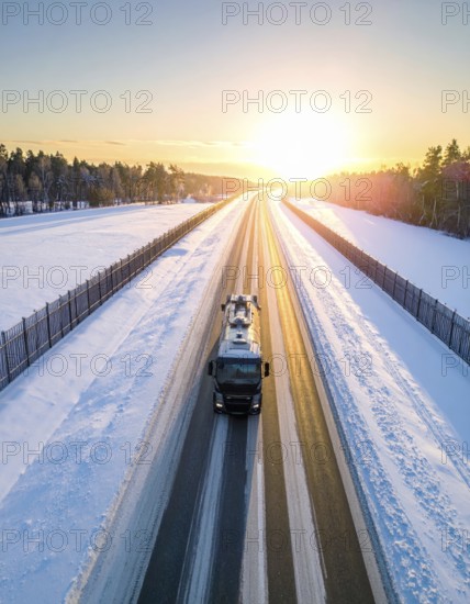 Petrol cargo truck lorry tanker driving on highway hauling oil products at sunrise, wide snowy landscape in winter, AI generated