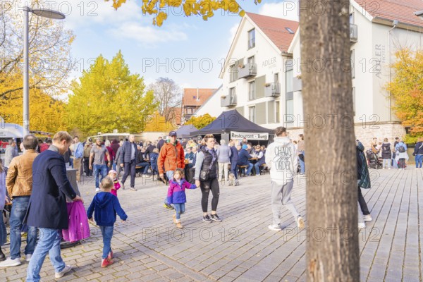 Families with children enjoy an autumnal day on a busy street with yellow trees, Urschelherbst Street Festival, Nagold, Germany