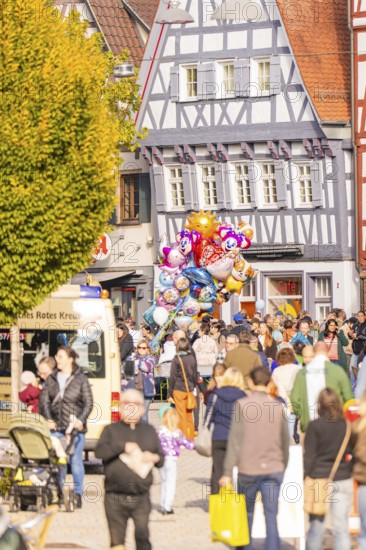 People pass half-timbered houses, colorful balloons over a lively crowd of roads, Urschelherbst street festival, Nagold, Germany