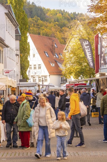 Families stroll across a busy market street under autumn leaves, Urschelherbst street festival, Nagold, Germany
