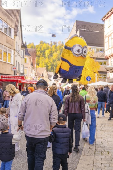 A minion balloon hovers over a family strolling through the city in sunny autumn, Urschelherbst street festival, Nagold, Germany