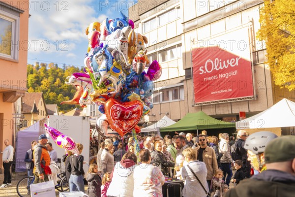 Colourful balloons over a crowd of people on a sunny market square surrounded by buildings, Urschelherbst street festival, Nagold, Germany