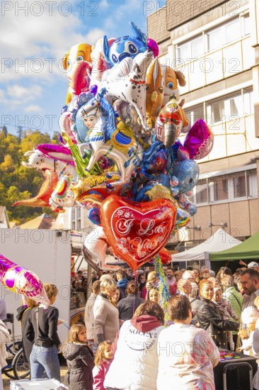 Various colorful balloons, including a heart with 'I Love You, 'float above a celebratory crowd, Urschelherbst street festival, Nagold, Germany