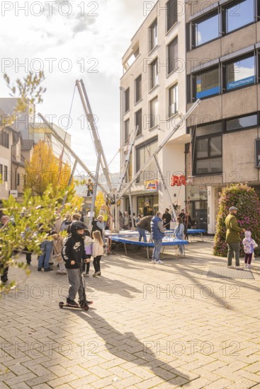 A group of people gather around bungee trampolines in an urban area, Urschelherbst Street Festival, Nagold, Germany