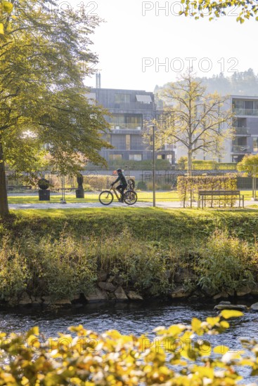 A cyclist rides through a park next to a river on a sunny autumn day, Urschelherbst Street Festival, Nagold, Germany