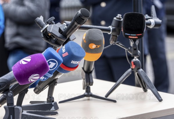 Microphones from various radio stations, television stations, standing on the table, at a press conference